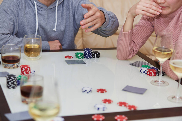 Мужчина и женщина играют в покер. Чипсы, открытки, бокалы виски и шампанское на столе с отражением. Фотография образа жизни. Ночь покера. - Фото, изображение