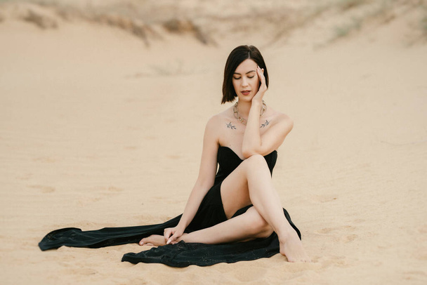 meisje in een zwarte lange jurk in een zandige woestijn onder een blauwe lucht - Foto, afbeelding