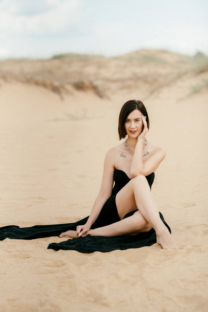 meisje in een zwarte lange jurk in een zandige woestijn onder een blauwe lucht - Foto, afbeelding