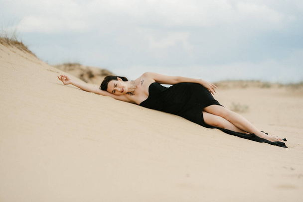 Mädchen im schwarzen langen Kleid in einer Sandwüste unter blauem Himmel - Foto, Bild