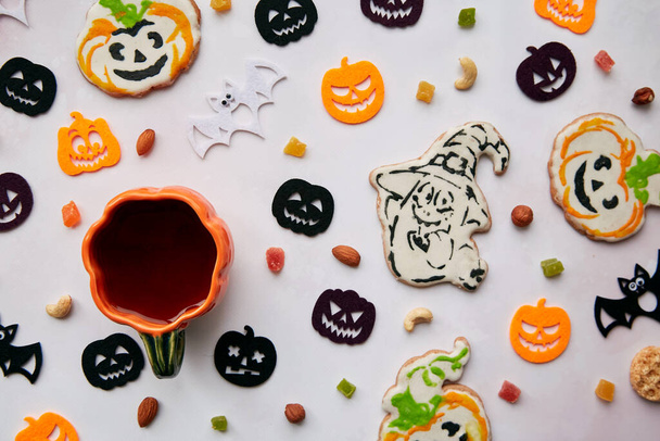 Homemade pumpkin and ghost cookies, Halloween felted decorations with nuts and candied fruits. Autumn holidays concept, Trick or treat. Cup of tea in shape of pumpkin. High quality photo.  - Photo, Image
