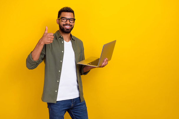 Photo of cute cheerful guy dressed green shirt eyewear thumb up reading modern gadget empty space isolated yellow color background - Photo, image