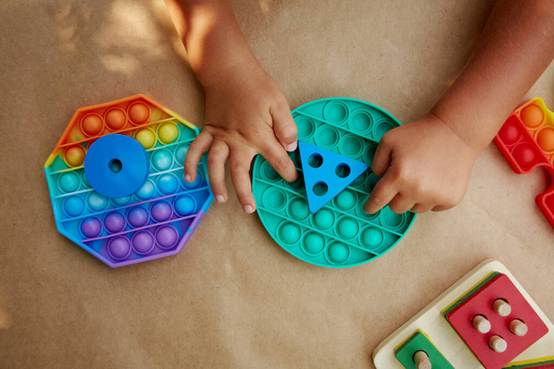 Babyhände spielen mit buntem Antistress-sensorischen Spielzeug Fidget Push. Trendiges Pop-it-Spielzeug zur Entwicklung der Feinmotorik. Regenbogensensorik zappelt. Neues trendiges Silikonspielzeug und Öko-Holzspielzeug. Hochwertiges Foto - Foto, Bild