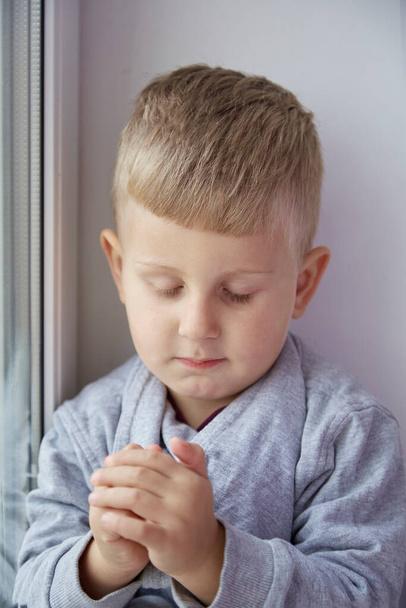 Πορτρέτο του μικρού αγοριού σε θέση προσευχής με σφιγμένα χέρια με κλειστά μάτια. . Υψηλής ποιότητας φωτογραφία - Φωτογραφία, εικόνα