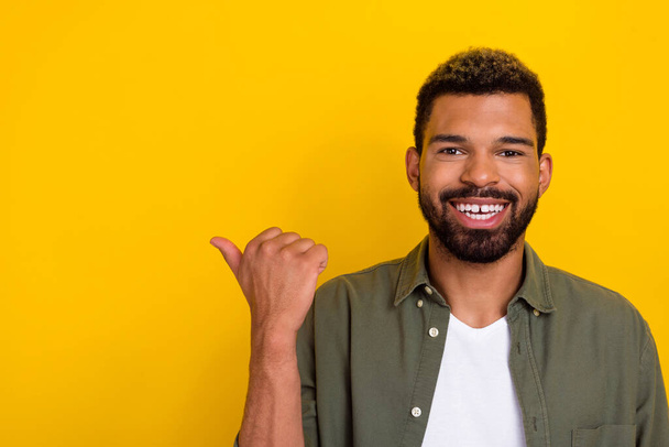 Photo of cheerful positive guy dressed green shirt pointing thumb empty space isolated yellow color background - 写真・画像
