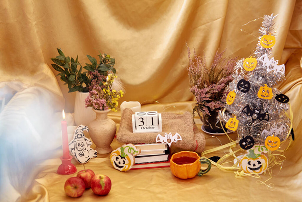 Ambiente de fiesta en casa con un moderno árbol de Halloween. Acogedoras decoraciones de Halloween con velas, taza de naranja, flores secas, galletas caseras en forma de calabaza y fantasma con libros y calendario - Foto, Imagen
