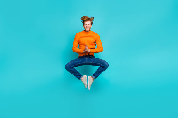 Full length photo of dreamy relaxing man wear orange pullover jumping high practicing yoga isolated teal color background - 写真・画像