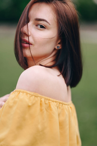 Retrato vertical de una hermosa chica de perfil, en un suéter amarillo con hombros desnudos y un pelo corto. Foto sin retoque. - Foto, imagen