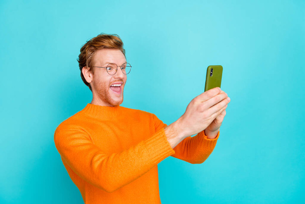 Photo of charming excited guy dressed orange sweater eyewear tacking photo modern device isolated turquoise color background - Foto, Bild