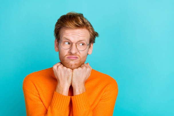 Photo of funny unsure young man wear orange pullover spectacles arms chin looking empty space isolated teal color background - Foto, afbeelding