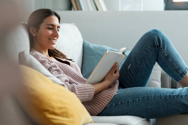 Shot of pretty young woman reading a book while sitting on sofa at home. - Foto, Imagem