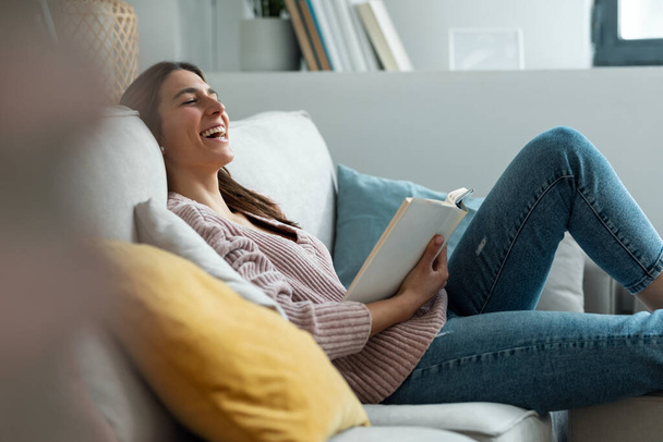 Shot of pretty young woman reading a book while sitting on sofa at home. - Foto, imagen