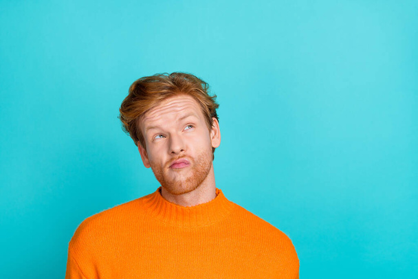 Photo of funky doubtful young man wear orange pullover looking empty space isolated teal color background - 写真・画像