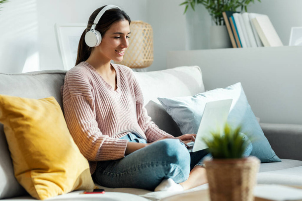 Shot of motivated young woman listening to music with laptop while singing and dancing sitting on sofa at home. - Zdjęcie, obraz