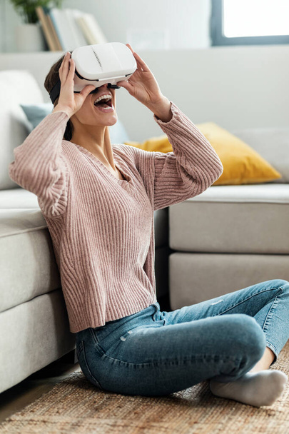 Shot of beautiful young woman using virtual reality headset and enjoying the moment sitting on the floor at home. - Foto, Bild