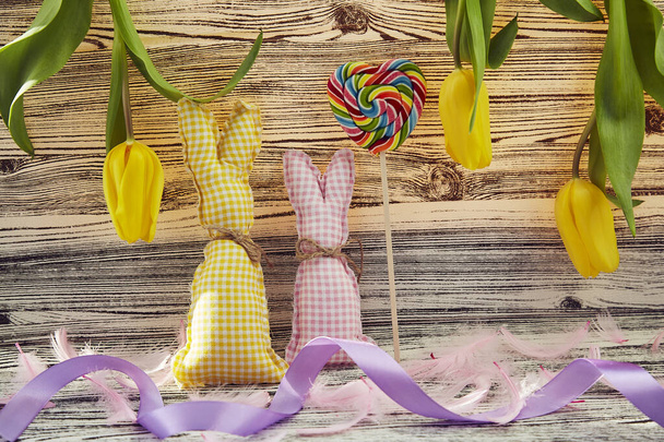 Fond de Pâques jaune avec des lapins faits à la main, tulipes jaunes, sucette en forme de coeur, plumes duveteuses roses. Printemps coloré créatif. Fond de Pâques. - Photo, image