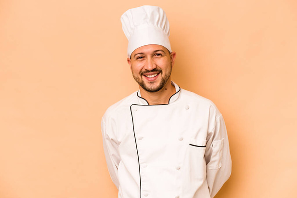 Chef hispano aislado sobre fondo beige feliz, sonriente y alegre. - Foto, Imagen