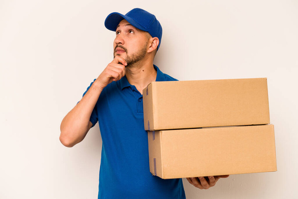 Hispanic delivery man isolated on white background looking sideways with doubtful and skeptical expression. - Photo, Image