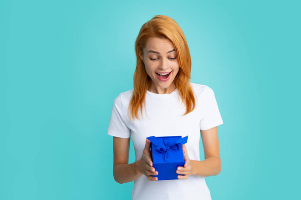 Happy birthday. Woman holding gift box with ribbon. Expressive facial expressions with suprised face. Studio portrait over blue background. - Foto, imagen