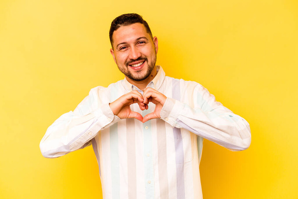 Fiatal spanyol férfi elszigetelt sárga háttér mosolygó és mutató szív alakú kezek. - Fotó, kép