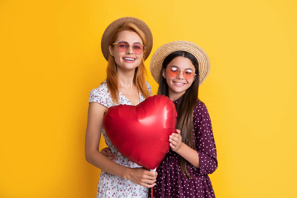 χαμογελαστή μητέρα και κόρη κρατώντας μπαλόνι καρδιά αγάπη σε κίτρινο φόντο - Φωτογραφία, εικόνα