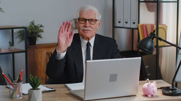 Senior business man waves hand palm in hi gesture greeting welcomes someone webinar at home office - Фото, изображение