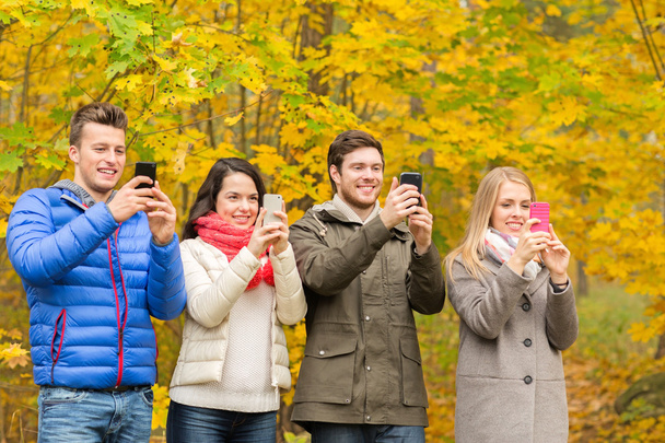 smiling friends with smartphones in city park - Foto, imagen