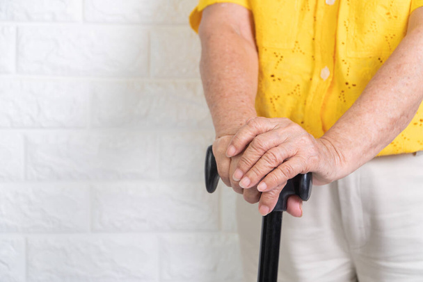 Ασιάτισσα ηλικιωμένη που κρατάει μπαστούνι σε απομονωμένο φόντο. Η έννοια της γηράσκουσας κοινωνίας που χρειάζεται χρόνο και εγγόνια για να επιστρέψει στη φροντίδα της υγείας - Φωτογραφία, εικόνα