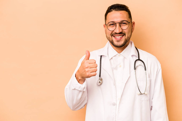 Hispanic doctor man isolated on beige background smiling and raising thumb up - 写真・画像