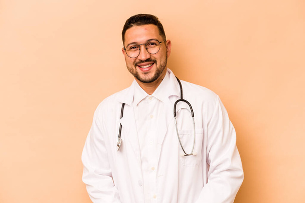 Hispánský lékař muž izolované na béžové pozadí šťastný, usmívající se a veselý. - Fotografie, Obrázek
