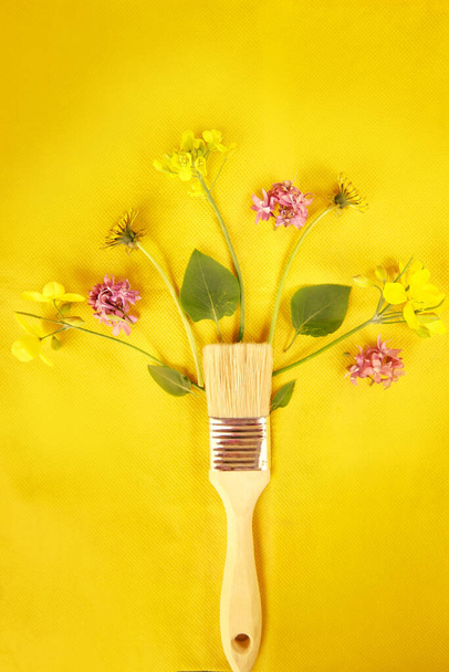 Splash of spring flowers from paint brush on yellow background. Sustainable, cottage core, connecting with nature concept. - Photo, Image