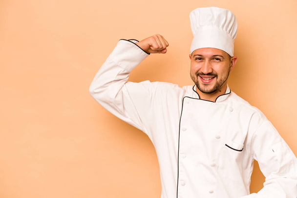 Chef hispano aislado sobre fondo beige levantando puño tras una victoria, concepto ganador. - Foto, imagen