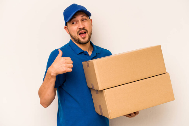 Hispanic delivery man isolated on white background points with thumb finger away, laughing and carefree. - Photo, Image