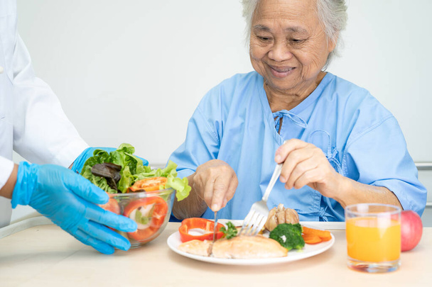 Asiatico anziani o anziani donna anziana paziente mangiare salmone bistecca colazione con verdura cibo sano mentre seduto e affamato sul letto in ospedale. - Foto, immagini