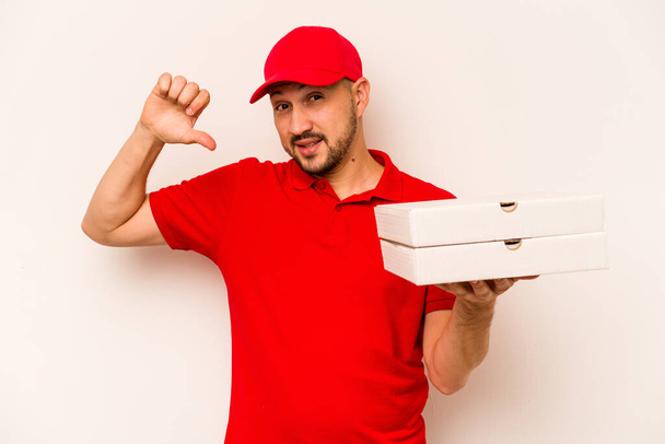 Young delivery man holding pizzas isolated on beige background feels proud and self confident, example to follow. - Zdjęcie, obraz