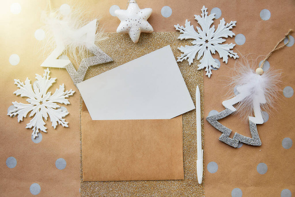 Бежевый, бумажная карточка, макет конверта, ручка. Модные рождественские украшения на основном фоне. Эстетическая праздничная атмосфера. Концепция отправки поздравительных открыток. Вид сверху. Место для текста - Фото, изображение