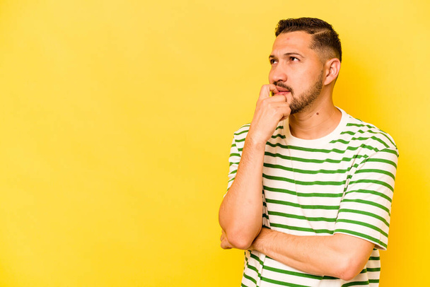 Young hispanic man isolated on yellow background relaxed thinking about something looking at a copy space. - Photo, Image