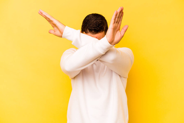 Молодой латиноамериканец, изолированный на жёлтом фоне, держит две руки скрещенными, концепция отрицания. - Фото, изображение