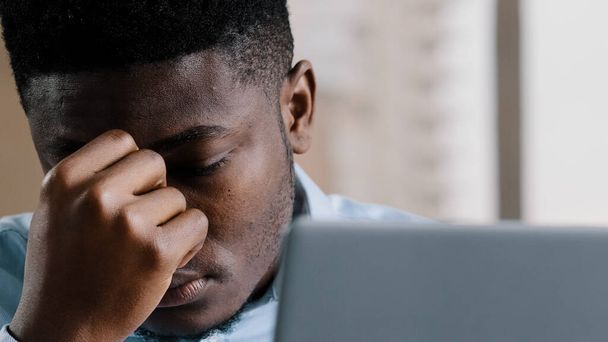 Close up exhausted young millennial african businessman overworked man massaging dry irritable eyes feeling eyestrain discomfort headache fatigue suffering from stress worrying problem bad news vision - 写真・画像