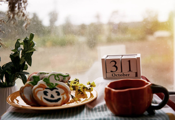 Happy Halloween still life with pumpkin cup and homemade cookies in shape of cute pumpkins and date of Halloween Day. Atmospheric aesthetic autumn holiday concept. Rural life. High quality photo - Photo, Image