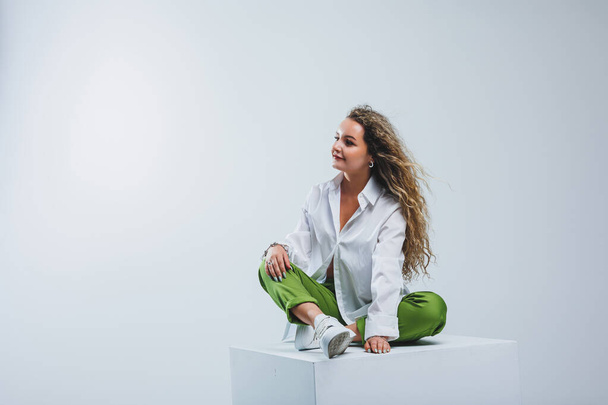 Positive woman with curly hair in a white light cotton shirt and trousers on a white isolated background. Women's casual wear. - Photo, Image