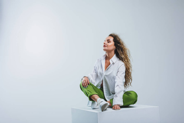 Positive woman with curly hair in a white light cotton shirt and trousers on a white isolated background. Women's casual wear. - Foto, Bild