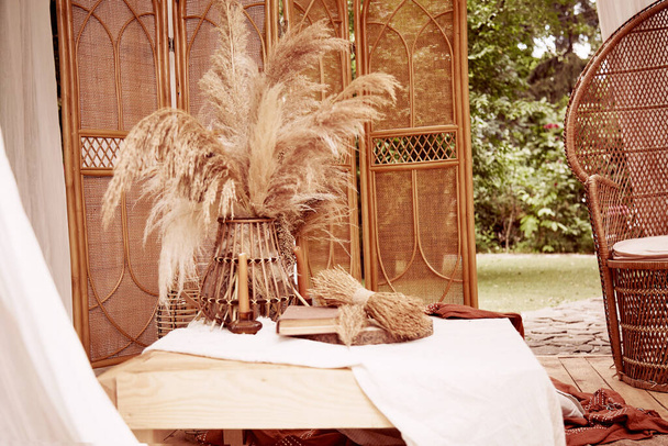 庭のインテリアのボヘミアンブーホスタイル。リネンのテーブルクロスにヴィンテージ本と乾燥葦の装飾とテーブルセッティング。結婚式の日のための審美的な装飾。高品質の写真 - 写真・画像