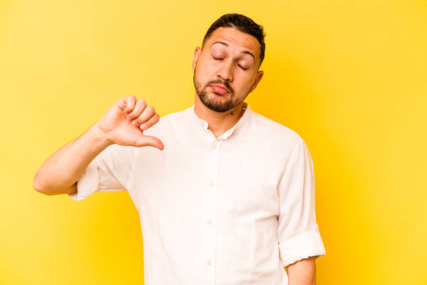 Молодий іспаномовний чоловік ізольований на жовтому тлі, показуючи нелюбимий жест, великі пальці вниз. Концепція розбіжностей
. - Фото, зображення