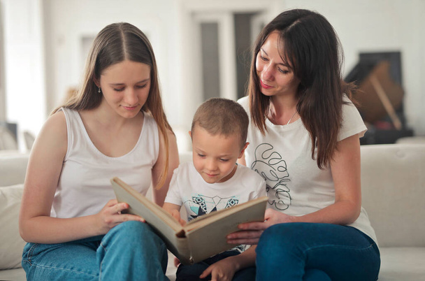mother and two children on the sofa at home look at a picture book - Foto, Bild