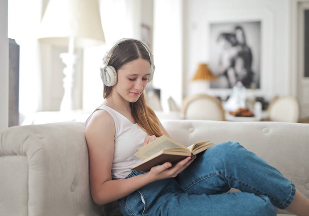Молодая девушка на диване читает книгу - Фото, изображение