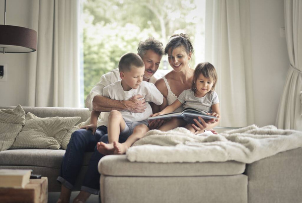 family sitting on a sofa looks at a picture book - Foto, imagen