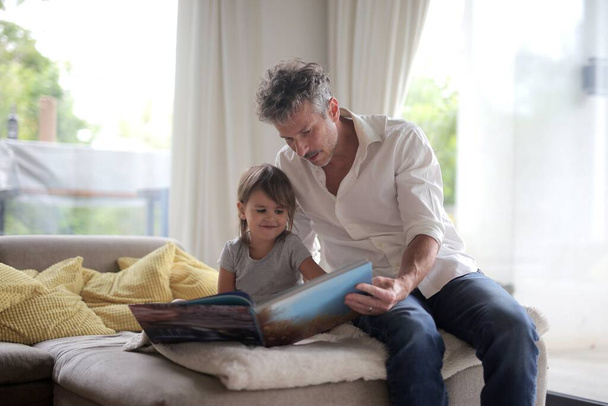 father and daughter on the sofa with a book - Photo, Image