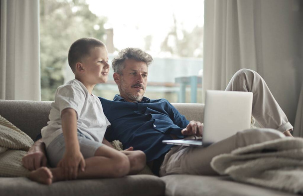 Baba ve oğul kanepede bilgisayar kullanıyorlar. - Fotoğraf, Görsel