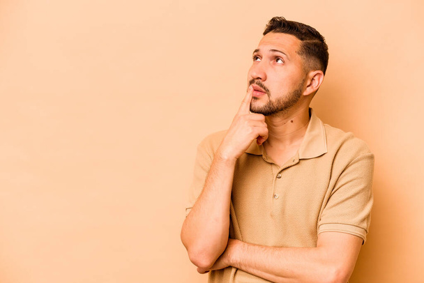 Young hispanic man isolated on beige background looking sideways with doubtful and skeptical expression. - Photo, Image
